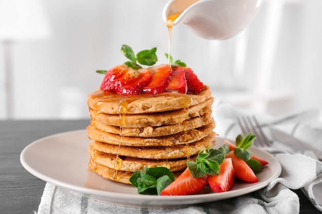 Verser la sauce sucrée de la saucière sur une pile de délicieuses crêpes à la noix de coco avec fraise et menthe