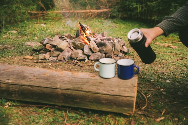 Verser le thé à la main dans des tasses en métal feu de camp sur fond