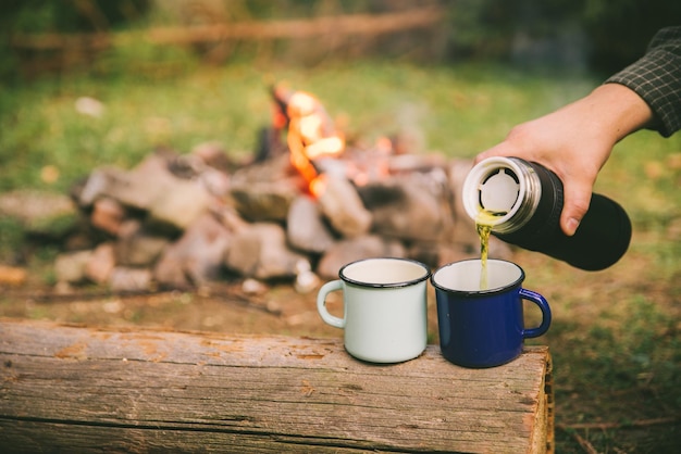 Verser le thé à la main dans des tasses en métal feu de camp sur fond