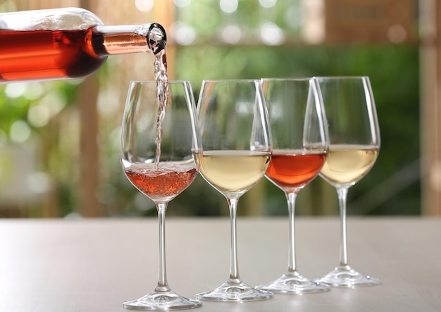 Verser le vin rosé de la bouteille dans le verre sur la table sur fond flou