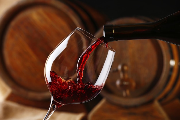 Verser le vin rouge de la bouteille dans le verre avec des fûts de vin en bois sur fond