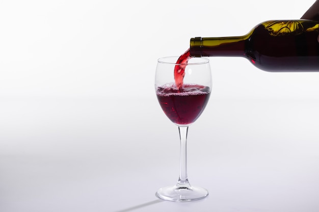Verser le vin rouge dans le verre sur fond blanc avec copie espace
