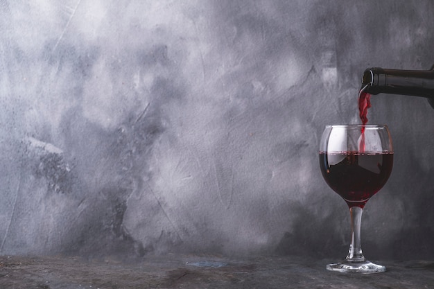 Photo verser le vin rouge dans le verre sur le mur gris. copyspace