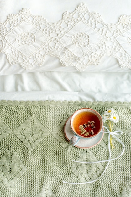 Verticale, plaid olive, tasse de tisane naturelle de menthe et mélisse au lit, matin se bouchent. Ambiance cosy Dentelle ajourée, couverture en coton blanc, fleurs de marguerite d'été. Style provençal et rétro.