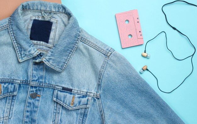 Veste en jean, cassette audio, écouteurs à vide sur une surface pastel bleue. Médias rétro, mélomane, années 80. Vue de dessus, pose à plat