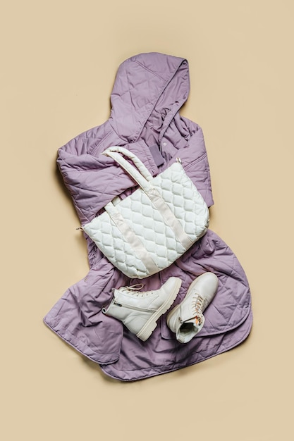 Veste oversize violette avec sac matelassé blanc et boots sur fond beige. Tenue de mode, style décontracté pour les jeunes, sport. Vêtements d'automne ou de printemps élégants.