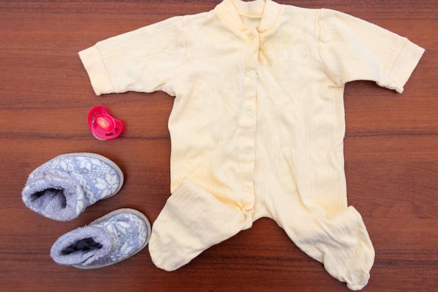 Vêtements de bébé, chaussons et sucette sur fond en bois. Kit pour nouveau-nés