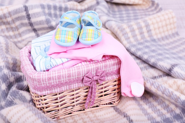 Photo vêtements de bébé dans le panier sur plaid dans la chambre