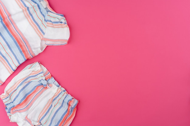 Vêtements bébé sur fond rose vue de dessus