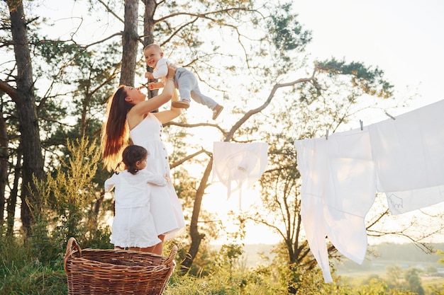 Vêtements blancs suspendus à la corde pour sécher Jeune mère avec sa petite fille et son fils est à l'extérieur dans la forêt Beau soleil