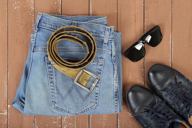 Vêtements chaussures et accessoires vue de dessus lunettes de soleil chaussures ceinture et jeans bleus sur fond en bois