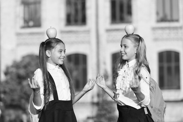 Vêtements d'école de filles souriantes avec des pommes sur le dessus de la tête concept d'enfants paisibles