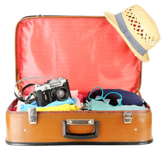 Des vêtements féminins et une caméra photo dans une vieille valise isolée sur blanc