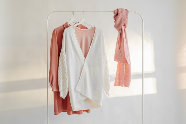Vêtements féminins de couleur rose pastel sur cintre sur fond blanc. Robe élégante, pull, chemise et écharpe. Garde-robe de maison de nettoyage de printemps. Notion minimale.