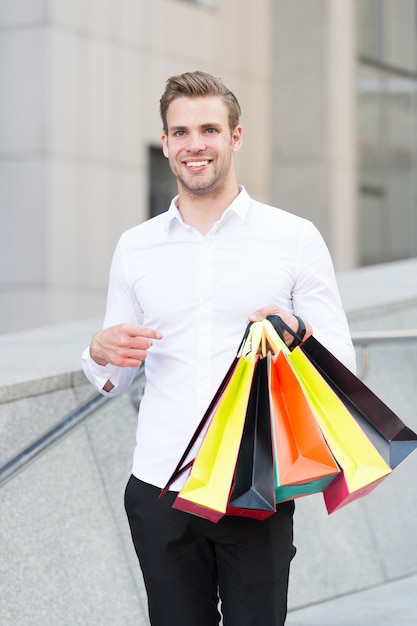 Les vêtements formels d'homme portent des sacs à provisions. Guy heureux porter des sacs à provisions. Offres avantageuses le vendredi noir. L'homme tient beaucoup de paquets de sacs en papier après avoir fait du shopping dans un centre commercial. Concept de vente de vendredi noir.