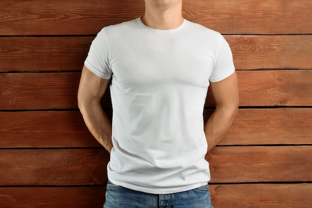 Vêtements de maquette. Homme en forme musculaire dans un T-shirt vierge et un jean bleu sur un fond de studio en bois marron. Modèle avant pour le design de mode.