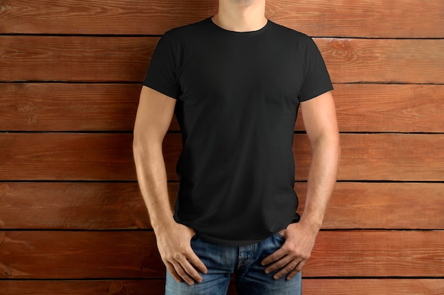 Vêtements de maquette. Homme mince de sport dans un T-shirt noir et un jean bleu sur un fond de studio en bois marron. Modèle prêt pour votre conception