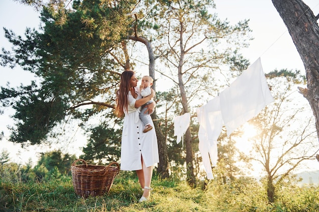 Des vêtements propres suspendus à la corde pour sécher Jeune mère avec son petit fils est à l'extérieur dans la forêt Beau soleil