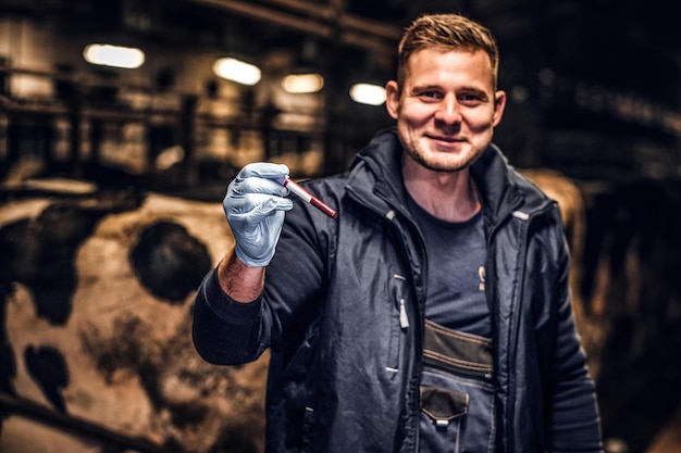 Un Vétérinaire Joyeux Tenant Un Tube à Essai Avec Un Liquide Rouge Sur Une Ferme De Vaches à L'intérieur