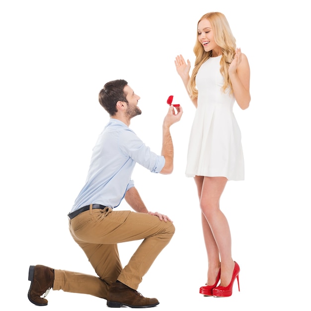 Photo veux-tu m'épouser? toute la longueur de l'homme faisant une proposition à sa petite amie tout en se tenant à ses genoux et en donnant une bague de fiançailles