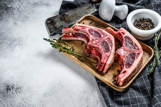 Viande d'agneau crue sur des côtes avec du romarin et des épices. Fond gris