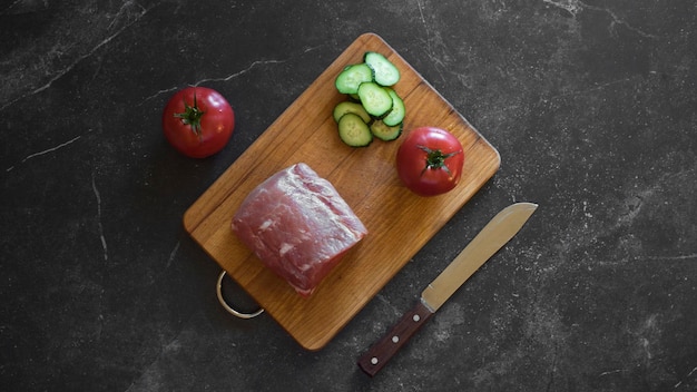 Viande aux concombres et tomates sur fond sombre avec un couteau alimentaire du haut