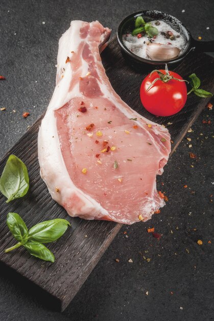 Viande biologique crue. Fond de cuisson des aliments. Porc sur os. Escalope pour frire les grillades. Avec des épices et des ingrédients basilic, ail, sur tableau noir sur fond de planche à découper en bois