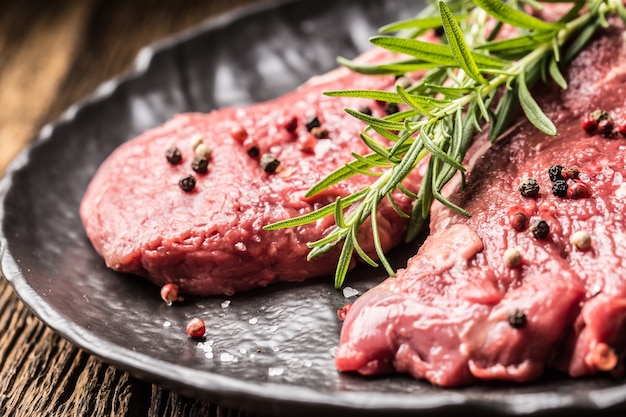 Viande de boeuf bifteck de faux-filet avec sel et poivre au romarin sur plaque noire.