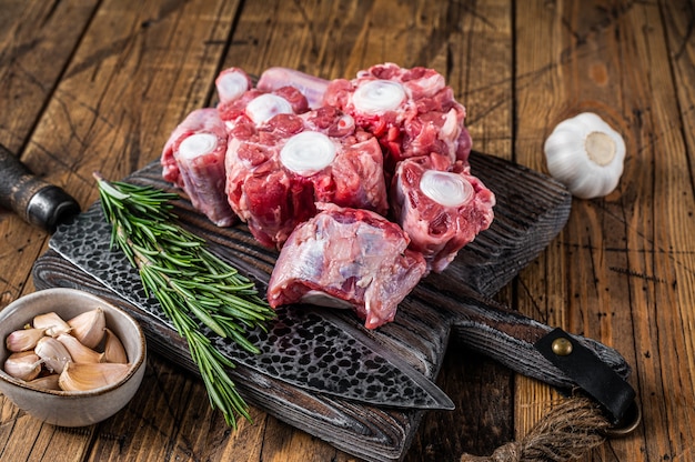 Photo viande de boeuf crue coupée en queue de bœuf sur une planche à découper en bois avec un couteau. fond en bois. vue de dessus.