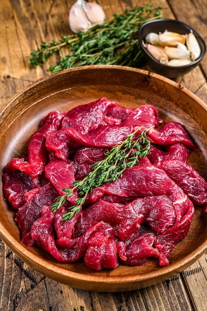 Viande de bœuf crue crue tranchée en lanières avec des herbes fraîches pour le bœuf stroganoff. table en bois. Vue de dessus.