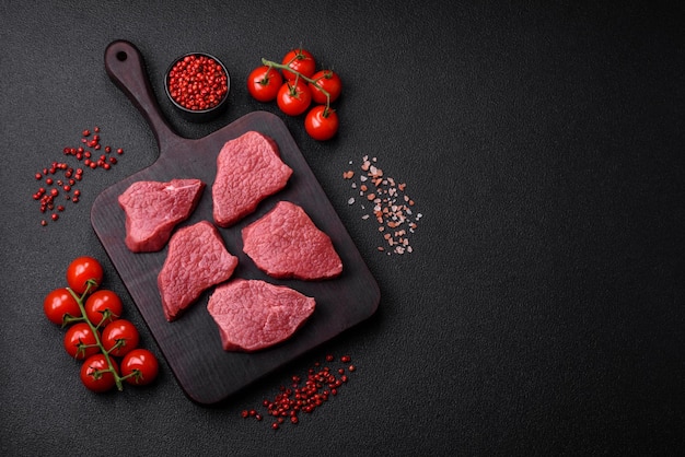 Viande de bœuf crue juteuse avec des épices salées et des herbes sur un fond en béton de texture sombre