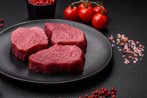 Viande de bœuf crue juteuse avec des épices salées et des herbes sur un fond en béton de texture sombre