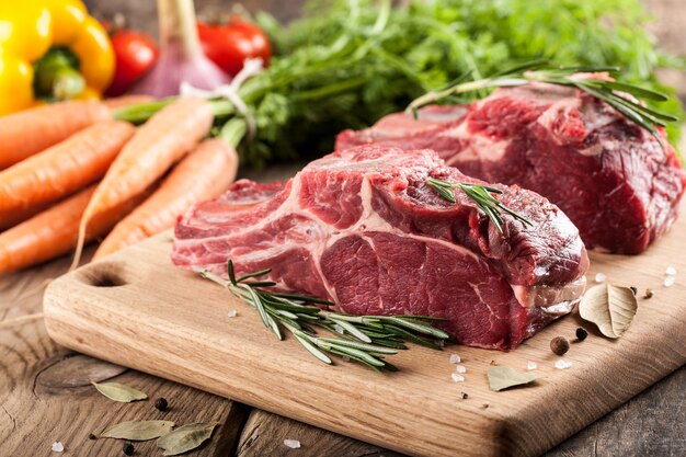 Viande de boeuf crue sur planche à découper et légumes frais sur table en bois