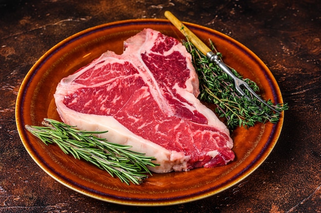 Viande de boeuf crue en T Steak aux herbes sur une assiette. Fond sombre. Vue de dessus.