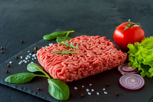 Viande de boeuf hachée crue sur une ardoise avec des feuilles et des épices.