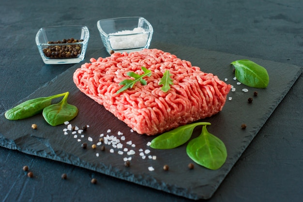 Viande de boeuf hachée crue sur une ardoise avec des feuilles et des épices.