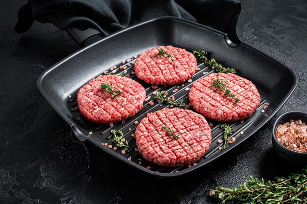 Viande de boeuf hachée crue Escalopes de steak de Burger dans une poêle à griller prête pour la cuisson Fond noir Vue de dessus