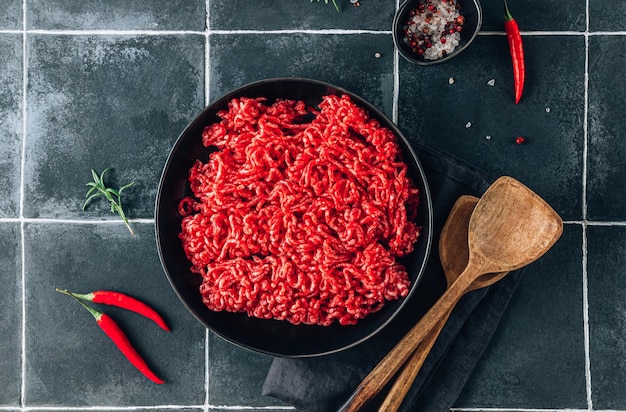 Viande de bœuf hachée crue fraîche avec des herbes et des épices sur assiette noire