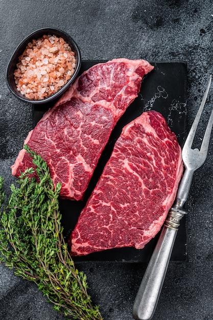 Viande de bœuf marbrée aux fines herbes. Fond noir. Vue de dessus.