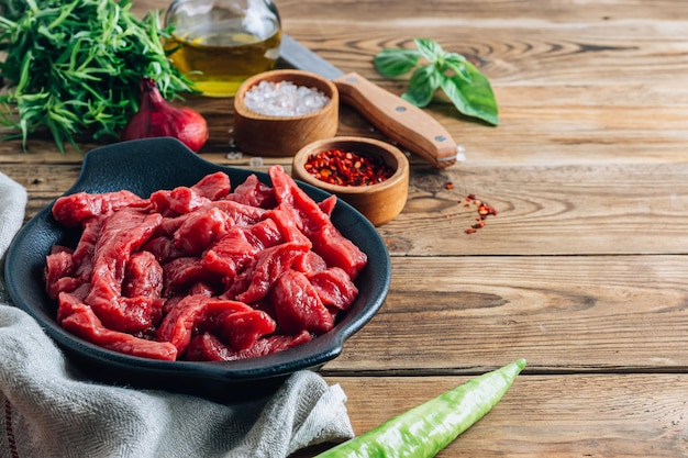 Viande de boeuf non cuite crue tranchée en lanières avec des ingrédients pour le boeuf stroganoff sur fond de bois rustique