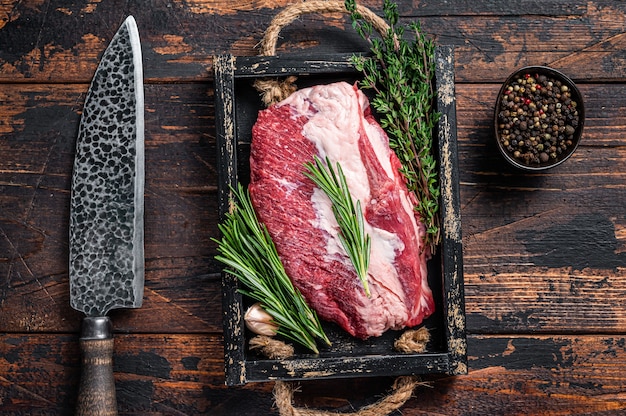 Viande de boeuf de poitrine crue coupée sur un plateau en bois avec un couteau. Bois foncé