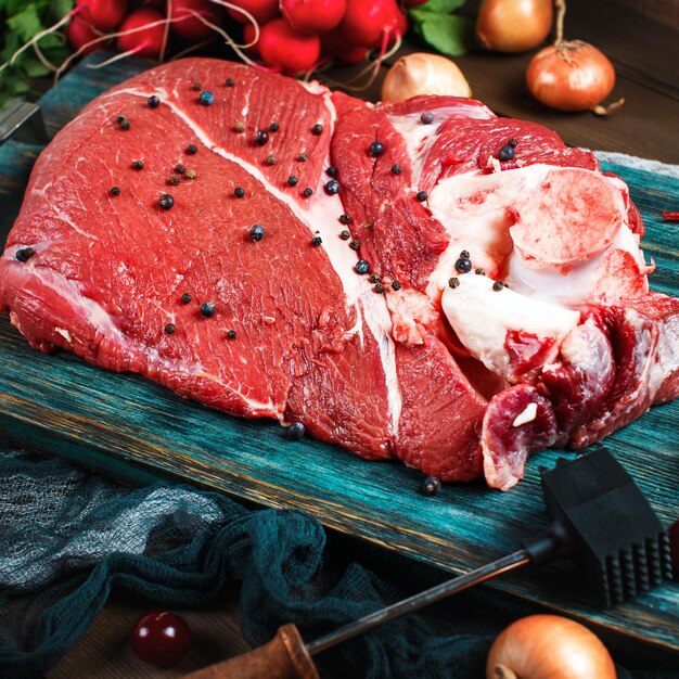 Photo viande de bœuf et de veau fraîche sur une table en bois rustique avec des ustensiles de cuisine et des légumes de composition carrée