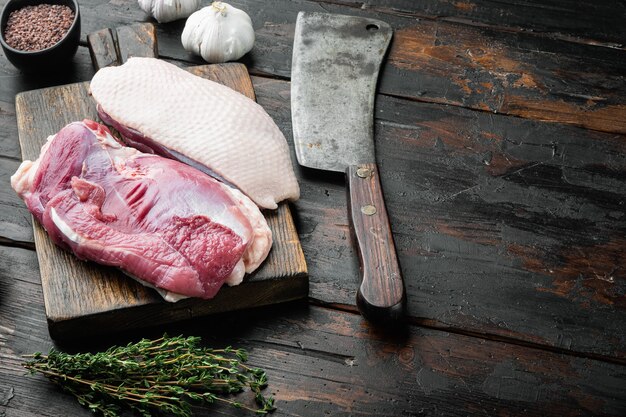 Photo viande de canard fraîche pour la nourriture, ensemble de poitrine de canard crue, sur une planche à découper en bois avec un vieux couteau de couperet de boucher, sur une vieille table en bois foncé