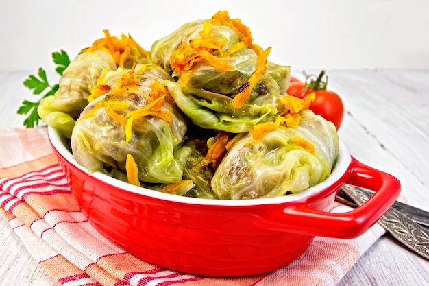 Viande de chou farcie dans des feuilles de chou avec des carottes rôties dans une rôtissoire sur une serviette rouge, tomates, couteau, fourchette sur un fond plus clair