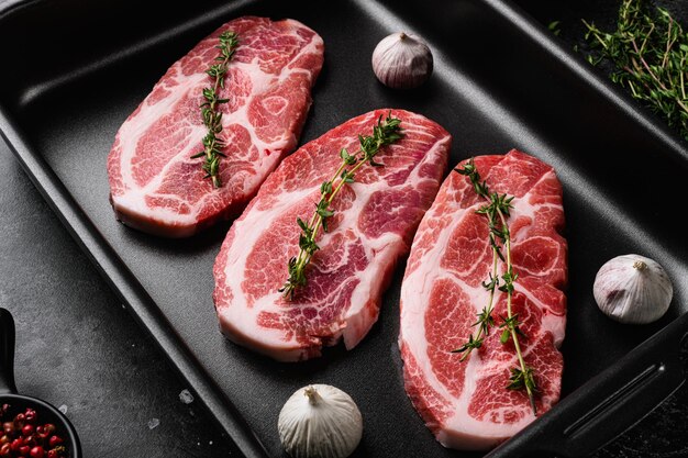 Viande de côtelette de cou de porc crue avec feuilles d'herbes et ensemble d'épices, sur fond de table en pierre noire foncée