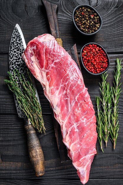 Viande de côtes courtes de veau de veau crue avec couteau de boucher. Fond en bois noir. Vue de dessus.