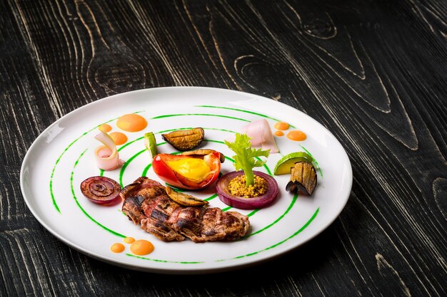 Viande coupée en tranches avec des légumes et des épices d'herbes fraîches d'un plat blanc sur un dessus en bois noir de fond...