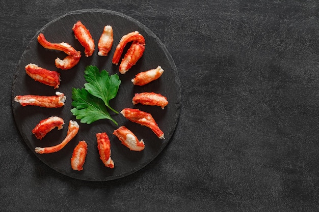 Viande de crabe en tranches de feuilles de persil vert cuit sur une plaque en pierre d'ardoise fond sombre vue de dessus espace pour copier du texte