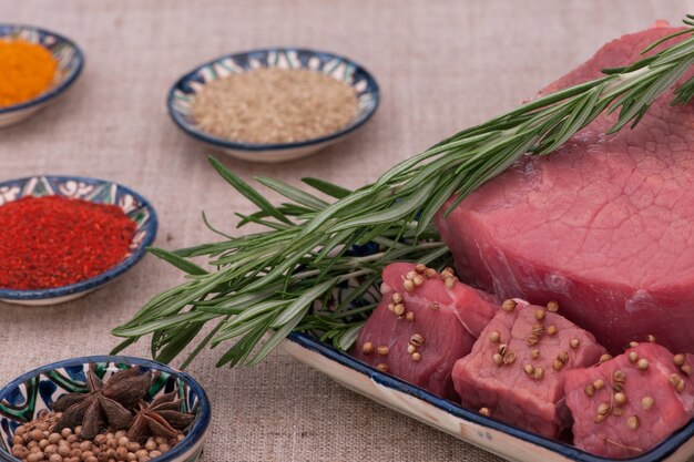 Viande crue aux épices et herbes dans une assiette carrée sur un tissu texturé