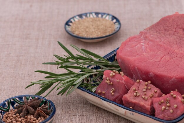 Viande crue aux épices et herbes dans une assiette carrée sur un tissu texturé